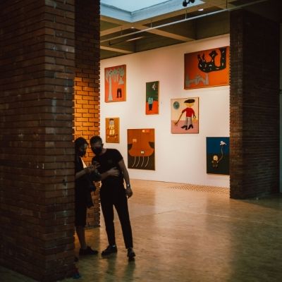 Wernisaż 9 Triennale Młodych, widok ogólny przestrzeni galerii, dwie postaci, na ścianie widzoczne obrazy- Zdjęcie udostępnione dzięki uprzejmości p. Piotra Czyża